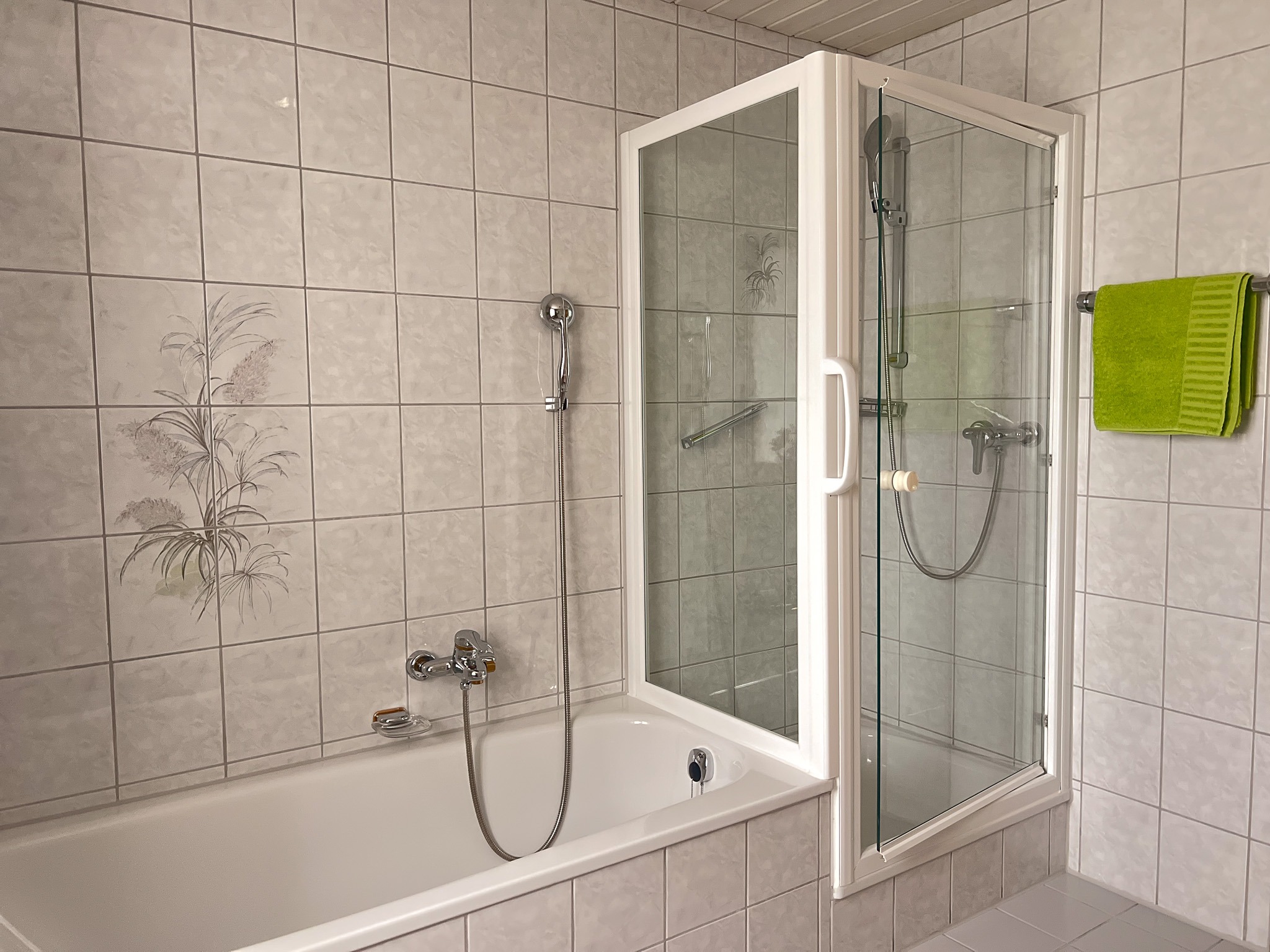 Klassische weiße Badewanne mit praktischer Glasduschwand und hellen Fliesen im Badezimmer.