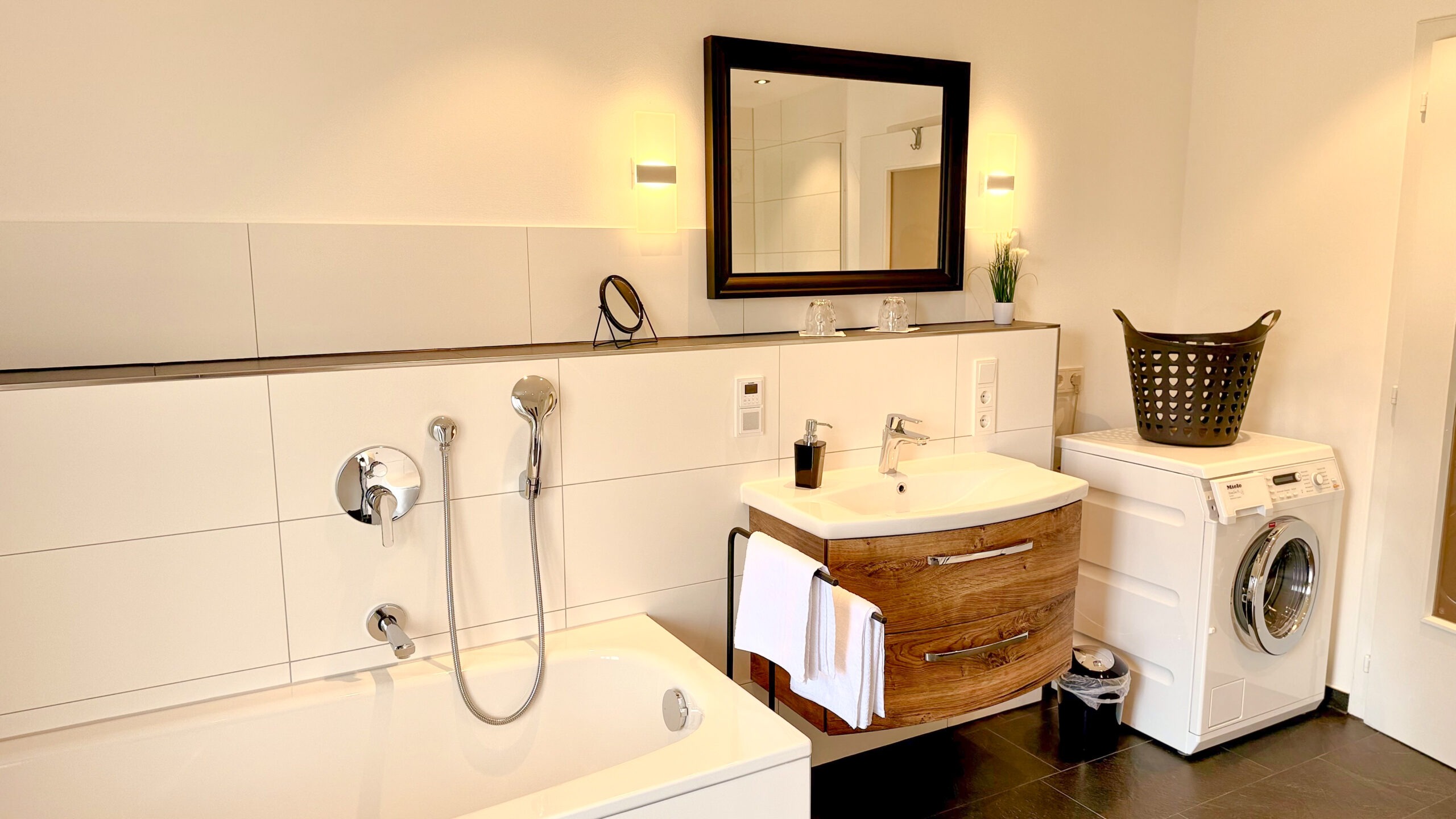 Ein geräumiges Badezimmer mit einer weißen Badewanne, einem Waschbecken mit Holzunterschrank und einer modernen Waschmaschine.