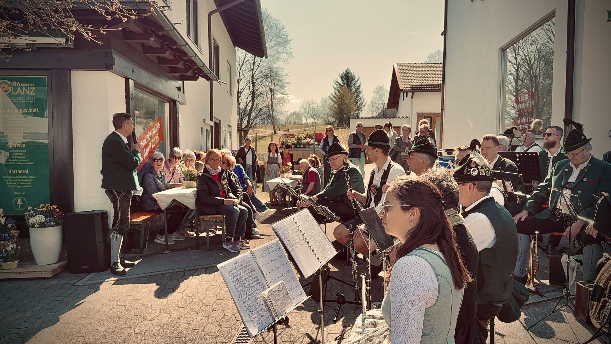 Eine bayerische Blaskapelle in traditioneller Tracht spielt an einem sonnigen Tag auf einem Platz in Bernau am Chiemsee für ein begeistertes Publikum.