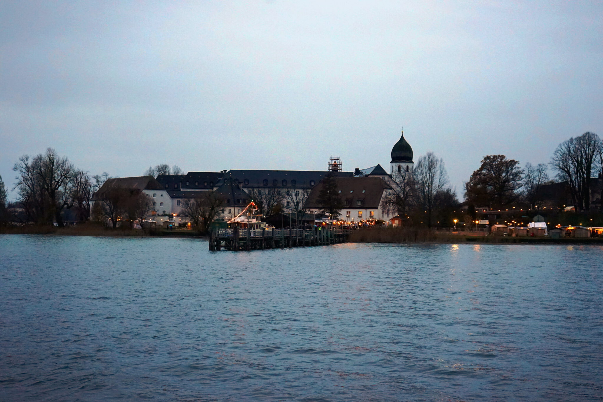 Festlich beleuchtete Weihnachtsbuden auf dem Christkindlmarkt der verschneiten Fraueninsel am Abend.