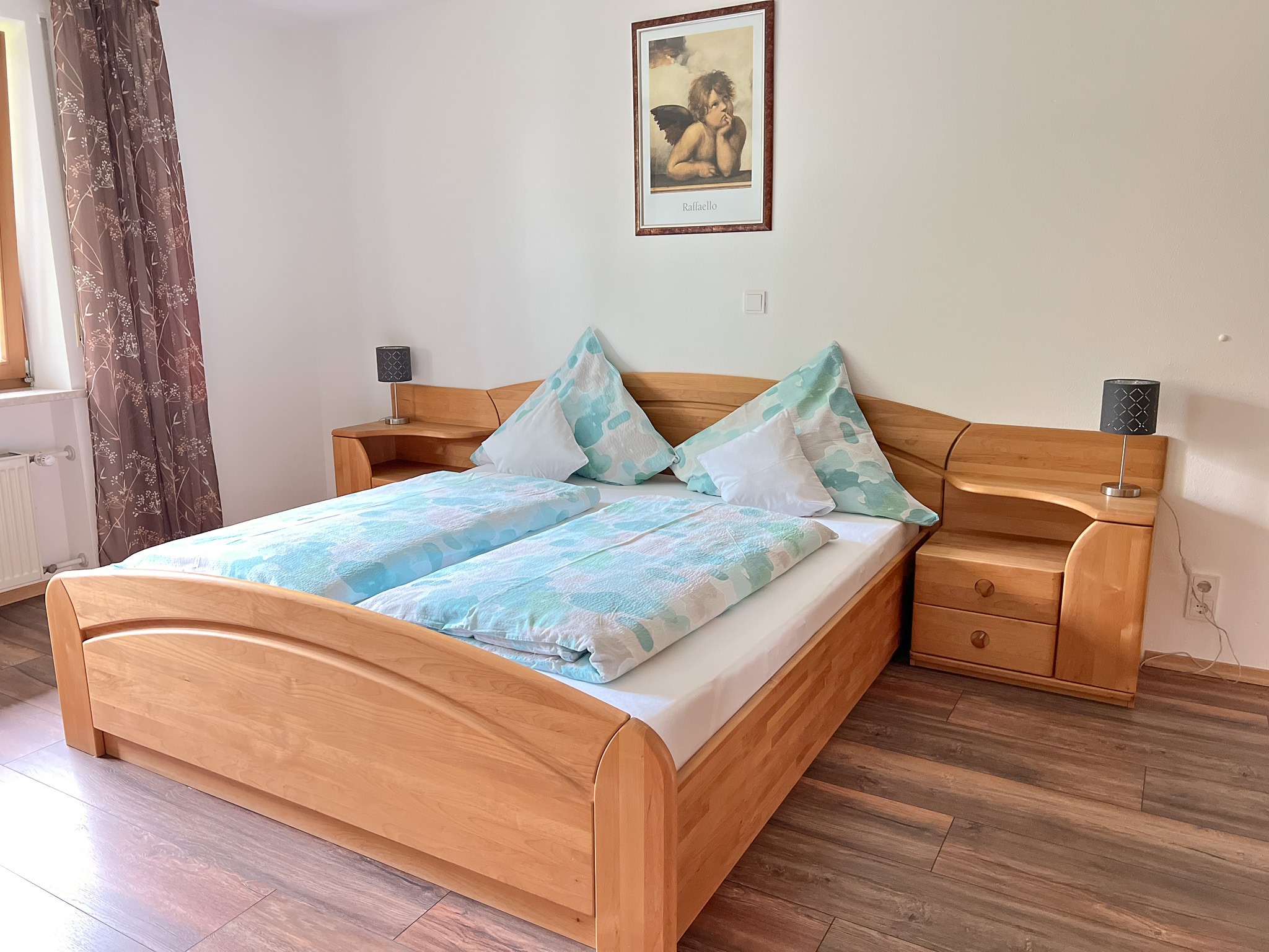 Gemütliches Doppelbett aus massivem Holz mit frischer blau-weißer Bettwäsche in einem hellen Schlafzimmer.