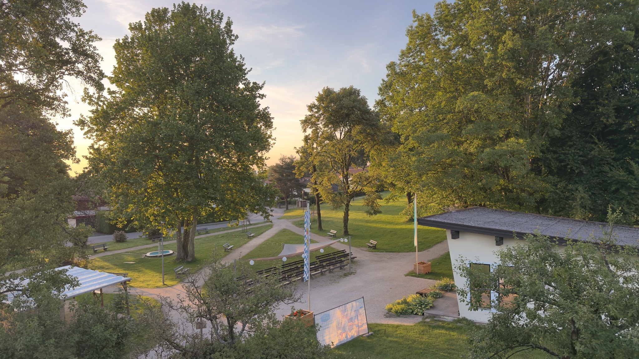 Gastgeber Ferienwohnung Bernau - Ein gepflegter Parkbereich in Bernau am Chiemsee mit großen, grünen Bäumen, Spazierwegen und einem modernen Gebäude im sanften Abendlicht.