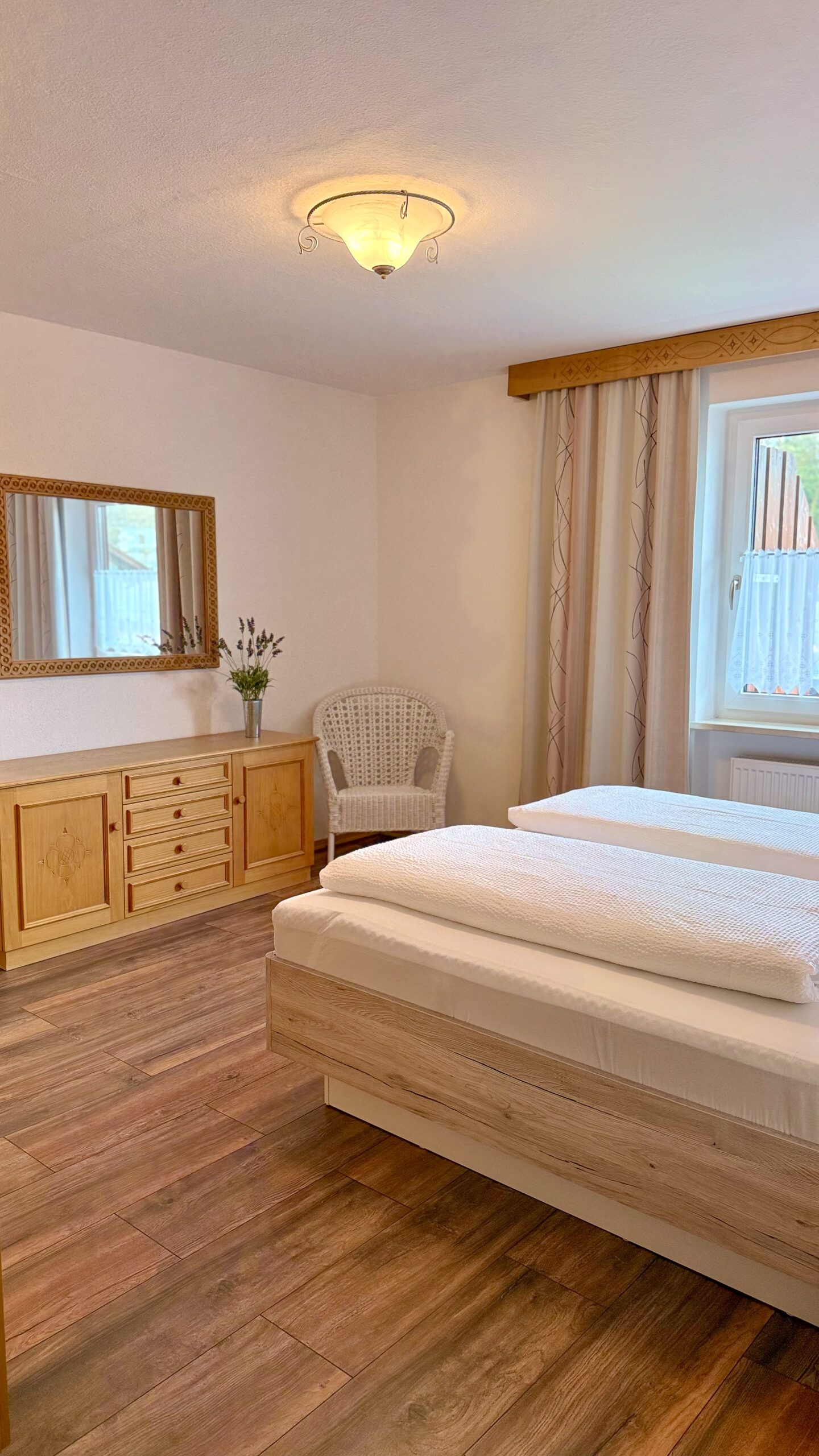 Ein gemütliches Schlafzimmer mit einem großen Doppelbett, warmem Holzfußboden, einer traditionellen Holzkommode und einem passenden Spiegel.