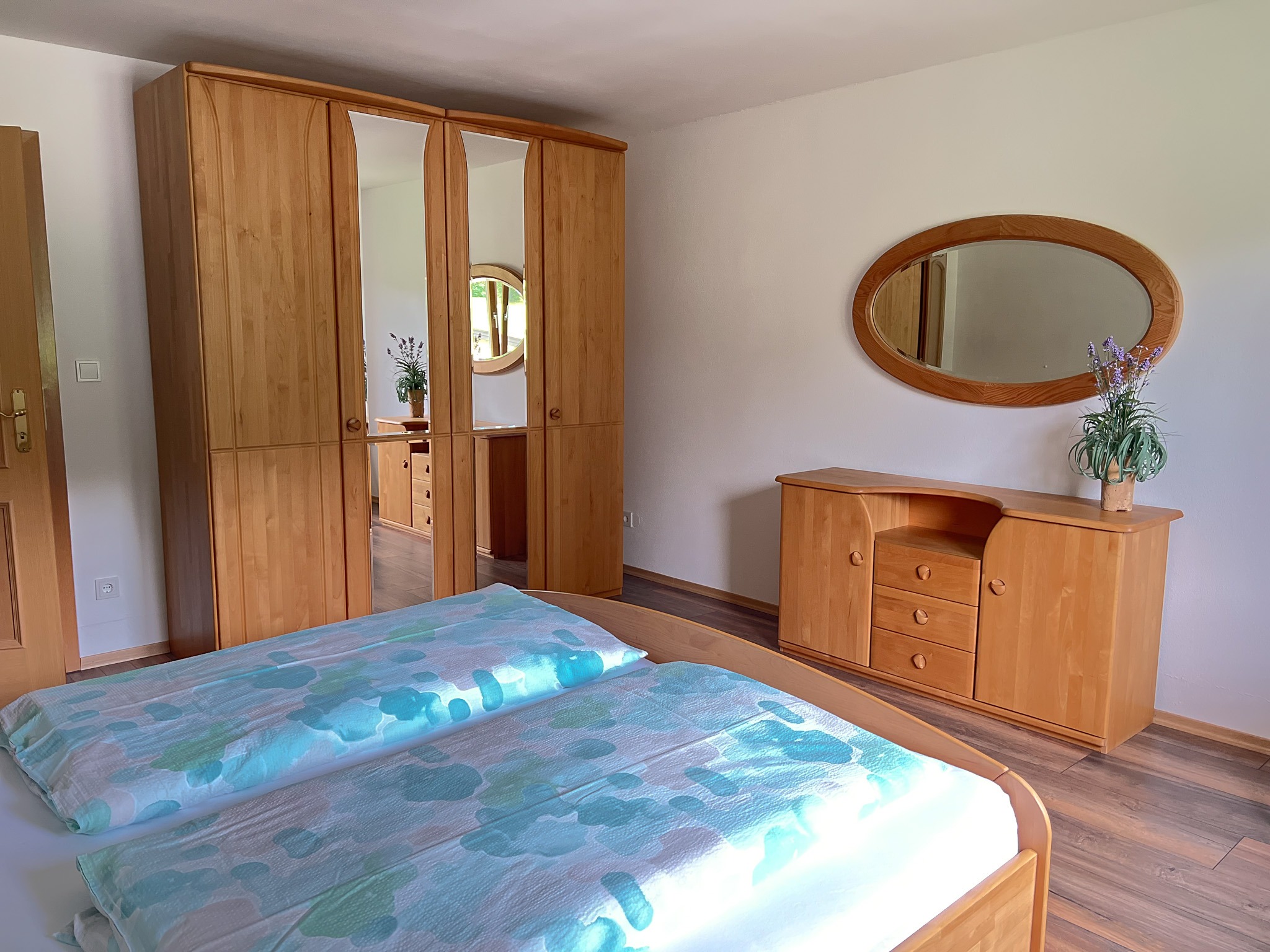 Großer Kleiderschrank aus Holz mit Spiegeltüren und eine passende Holzkommode im Schlafzimmer.