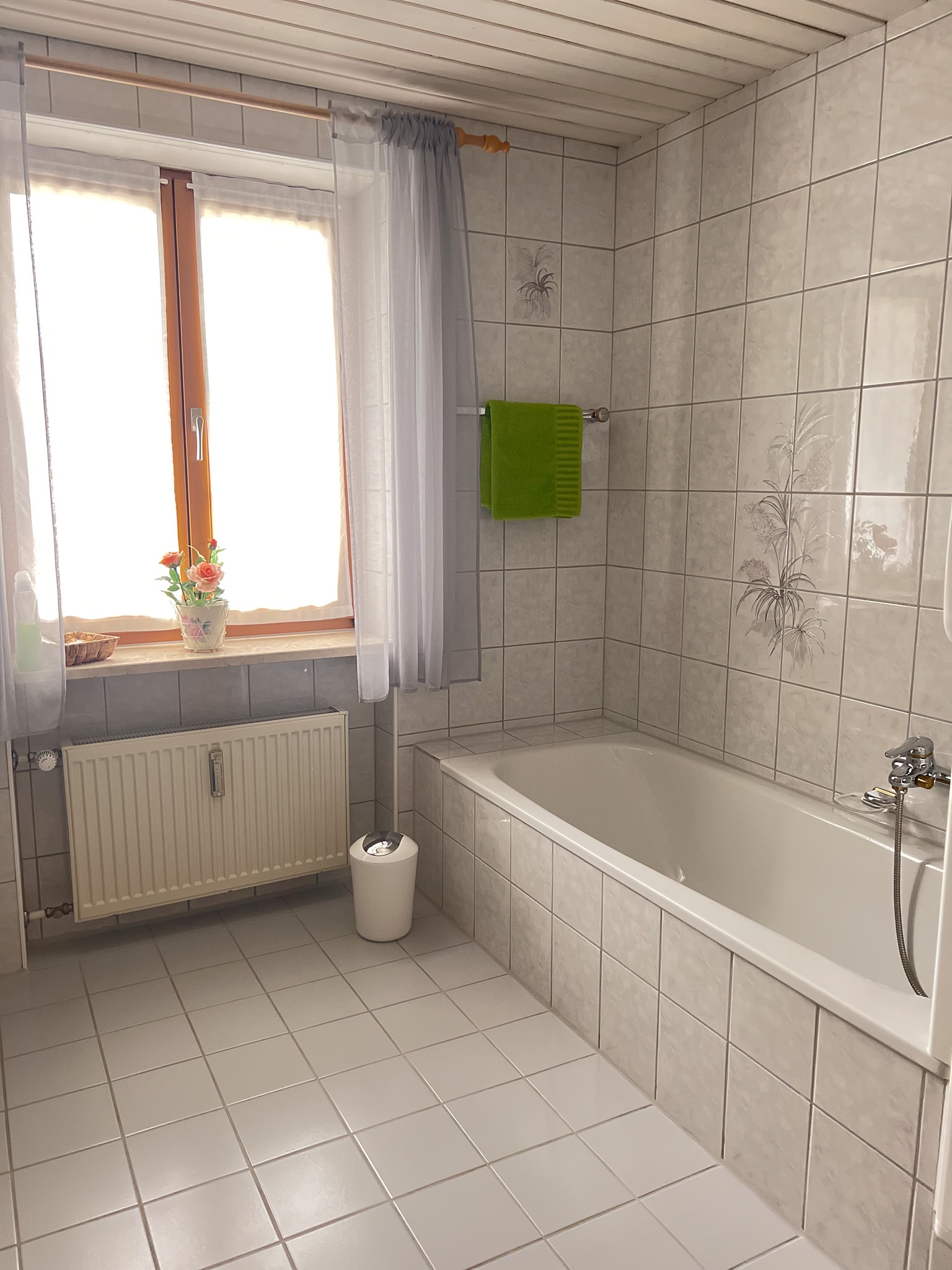 Badezimmer mit Badewanne, hellen Fliesen und einem großen Fenster, das viel Tageslicht hereinlässt.