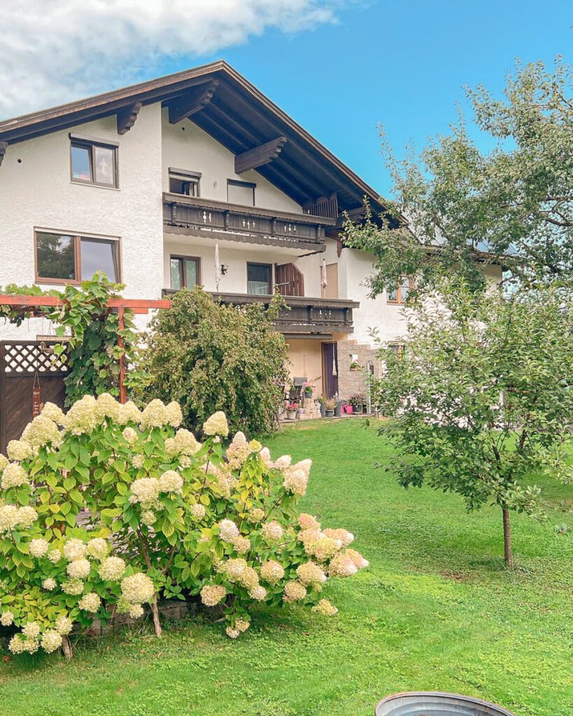 Außenansicht der Ferienwohnung am Chiemsee mit Holzbalkonen, blühenden Rispenhortensien und Garten mit Apfelbaum